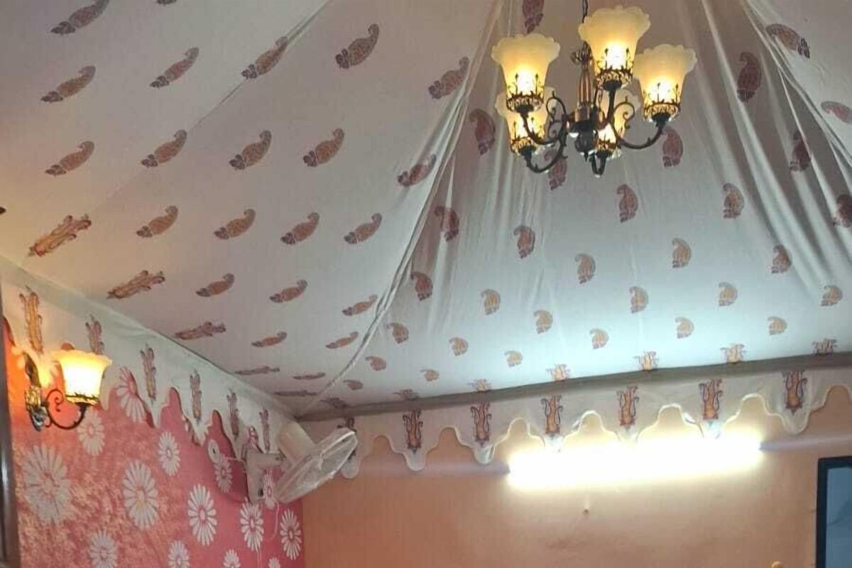 A bedroom with a bed, a patterned wall, a chandelier, and a door.