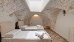 A cozy attic bedroom with two beds, a skylight, stone walls, and a radiator.