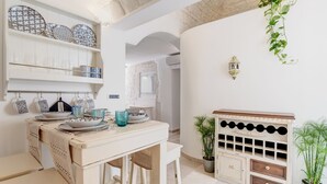 A kitchen with white cabinetry, a dining table with stools, and a cabinet with wine bottles.