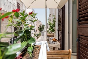 Un balcon avec une table dressée pour deux personnes, une chaise et un pot de fleurs.