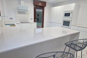 A modern kitchen with white cabinetry, a large island, and two bar stools. - 1A119 El Sangar Somio (Gijón)