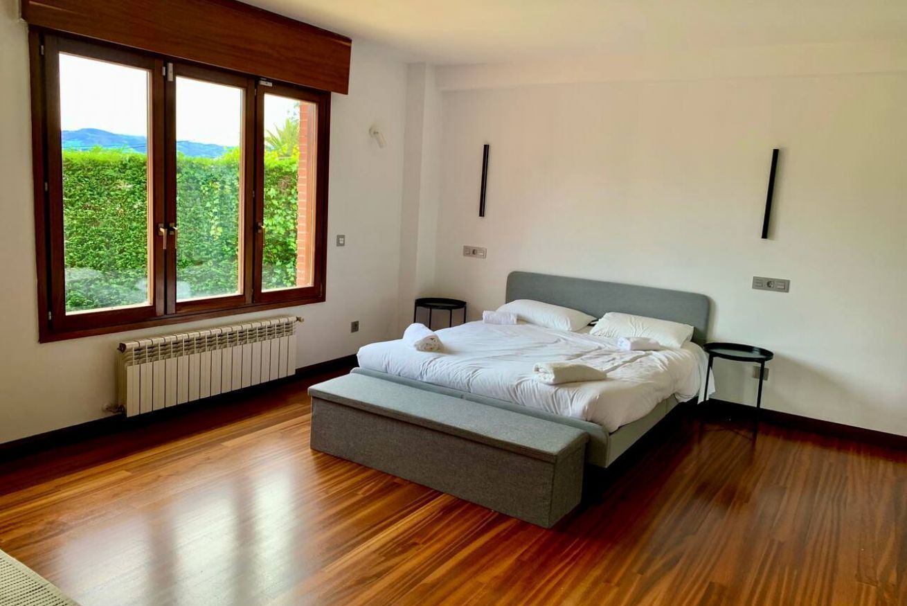 Quarto com uma janela grande, cama, banqueta e radiador.