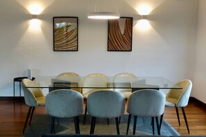 Een moderne eethoek met een glazen tafel, omringd door zes stoelen, twee wandlampen en abstracte kunst.