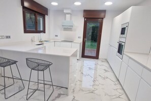 Een moderne keuken met een marmeren vloer, witte kasten, een ingebouwde oven en een groot eiland met krukken.