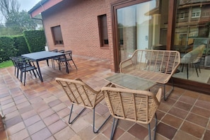 A patio with a table and chairs, a glass door, and a brick wall. - 1A119 El Sangar Somio (Gijón)