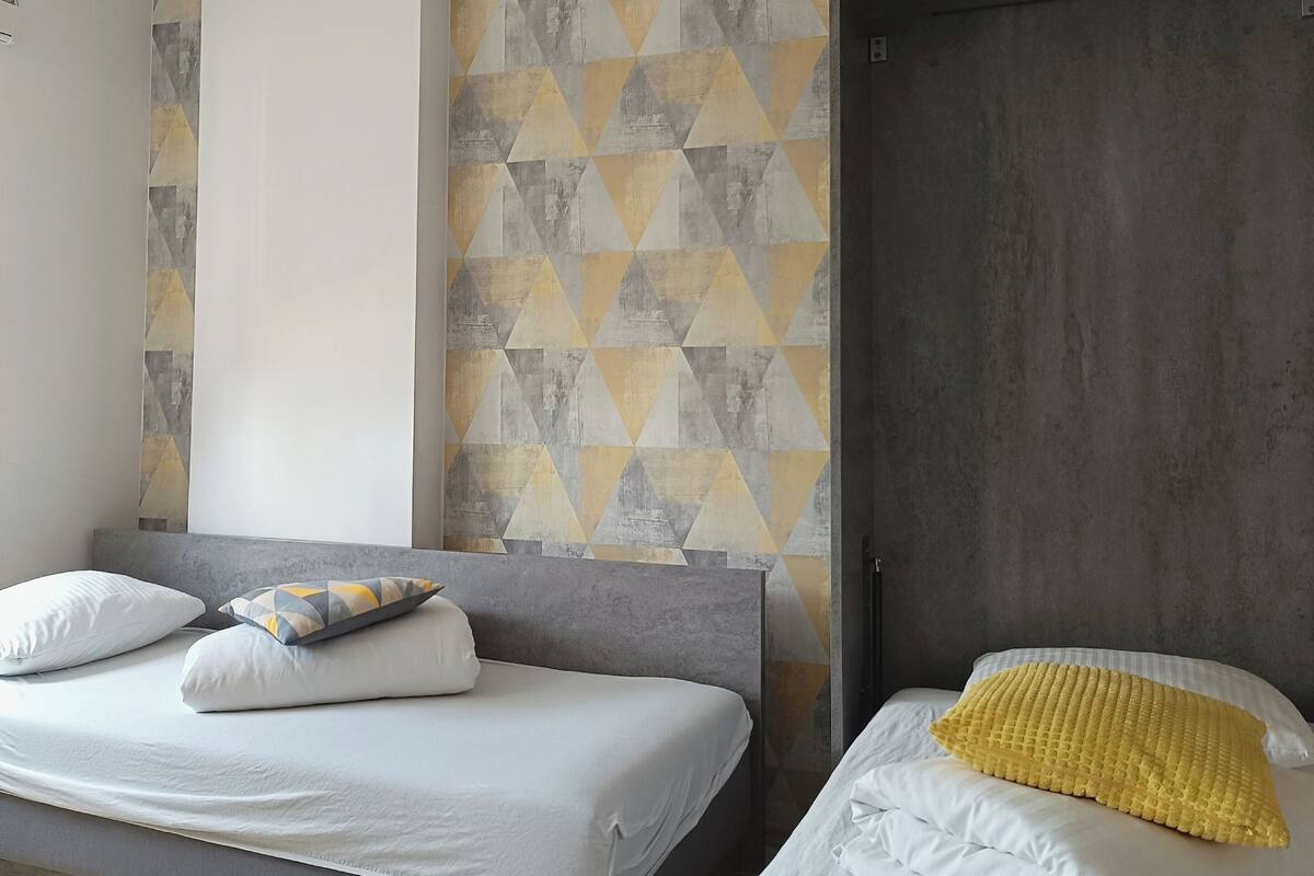 A modern hotel room with a large bed, a smaller bed, and a wardrobe.