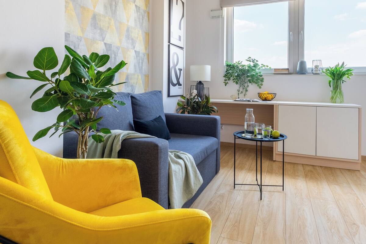 A modern living room with a sofa, a yellow armchair, a coffee table, and a window with a view.