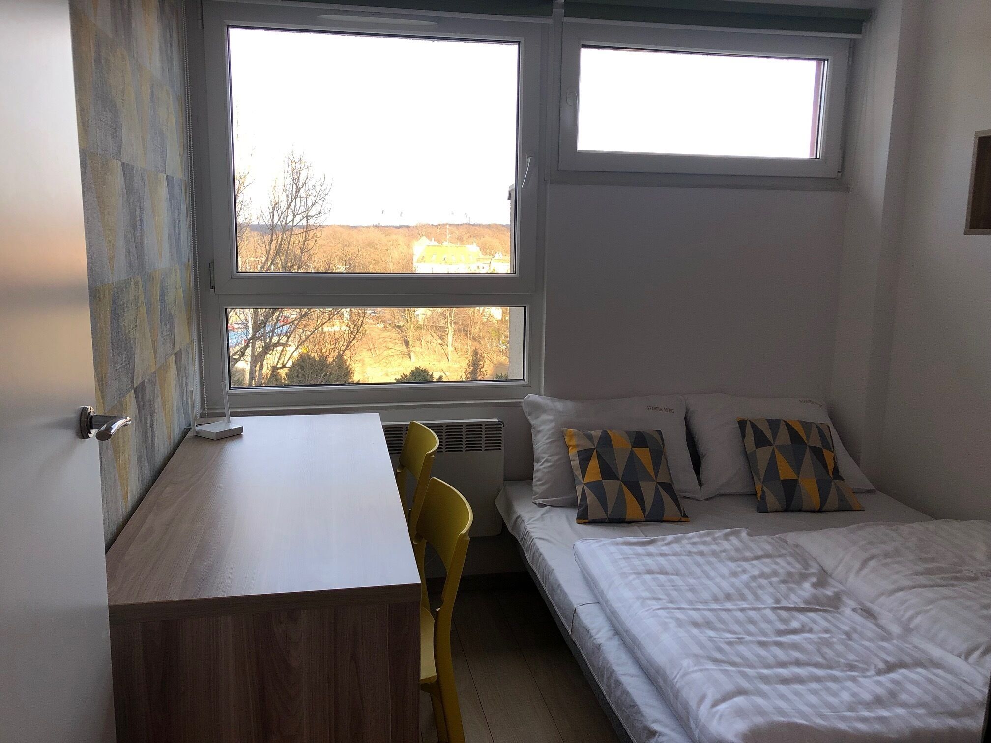 A bedroom with a bed, a desk, and two windows.
