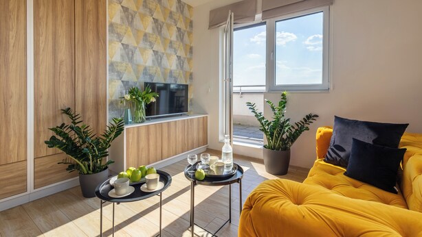 A modern living room with a yellow sofa, a TV, and a dining area with a tray of apples and glasses. - Starter Apart Wrocław (Wroclaw)