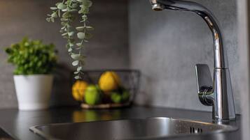 A kitchen sink with a modern faucet, a potted plant, and a bowl of lemons.