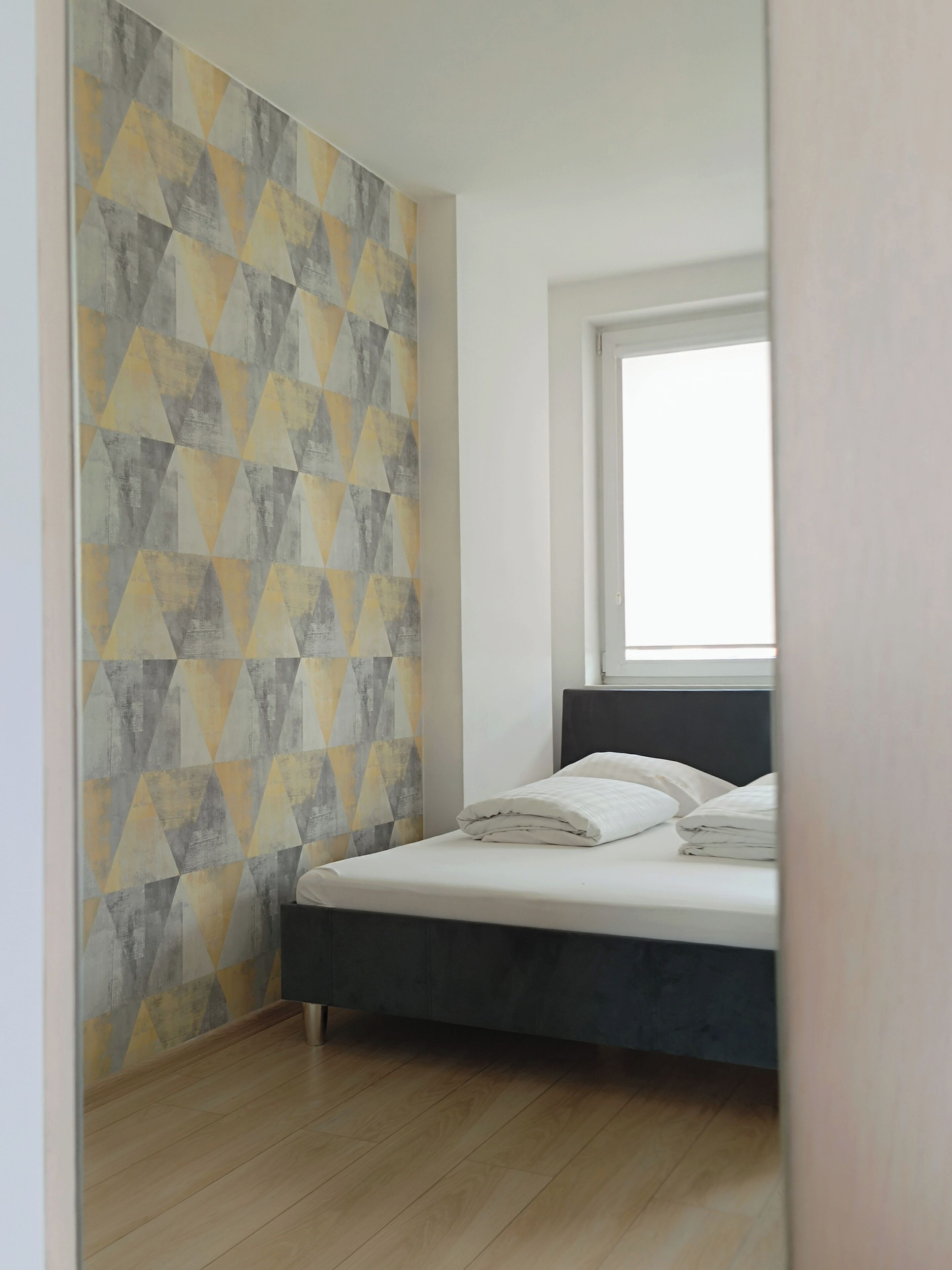 A bedroom with a bed, a window, and a geometric-patterned wall.