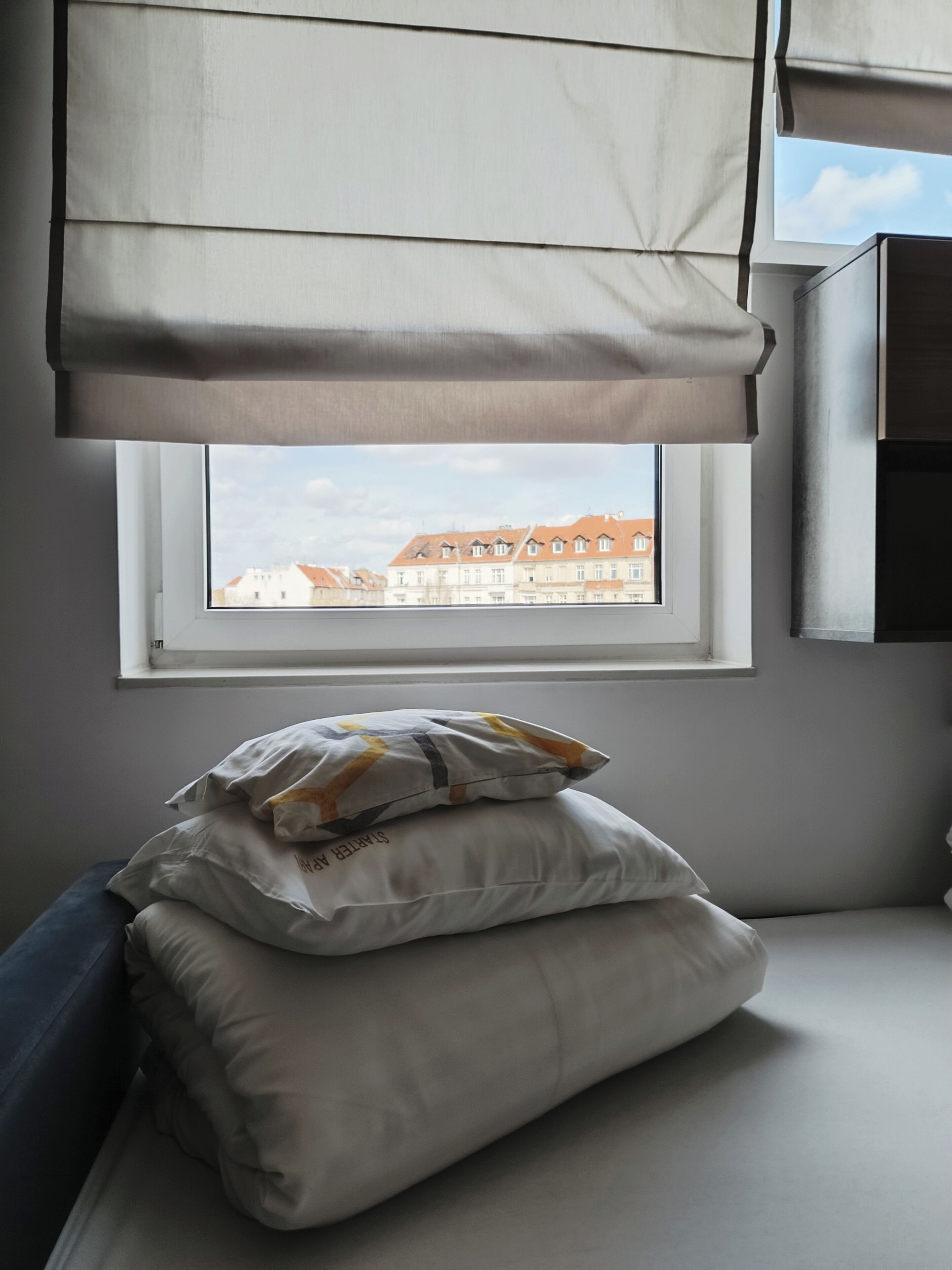 A bedroom with a window, a bed with pillows, and a wall-mounted cabinet.