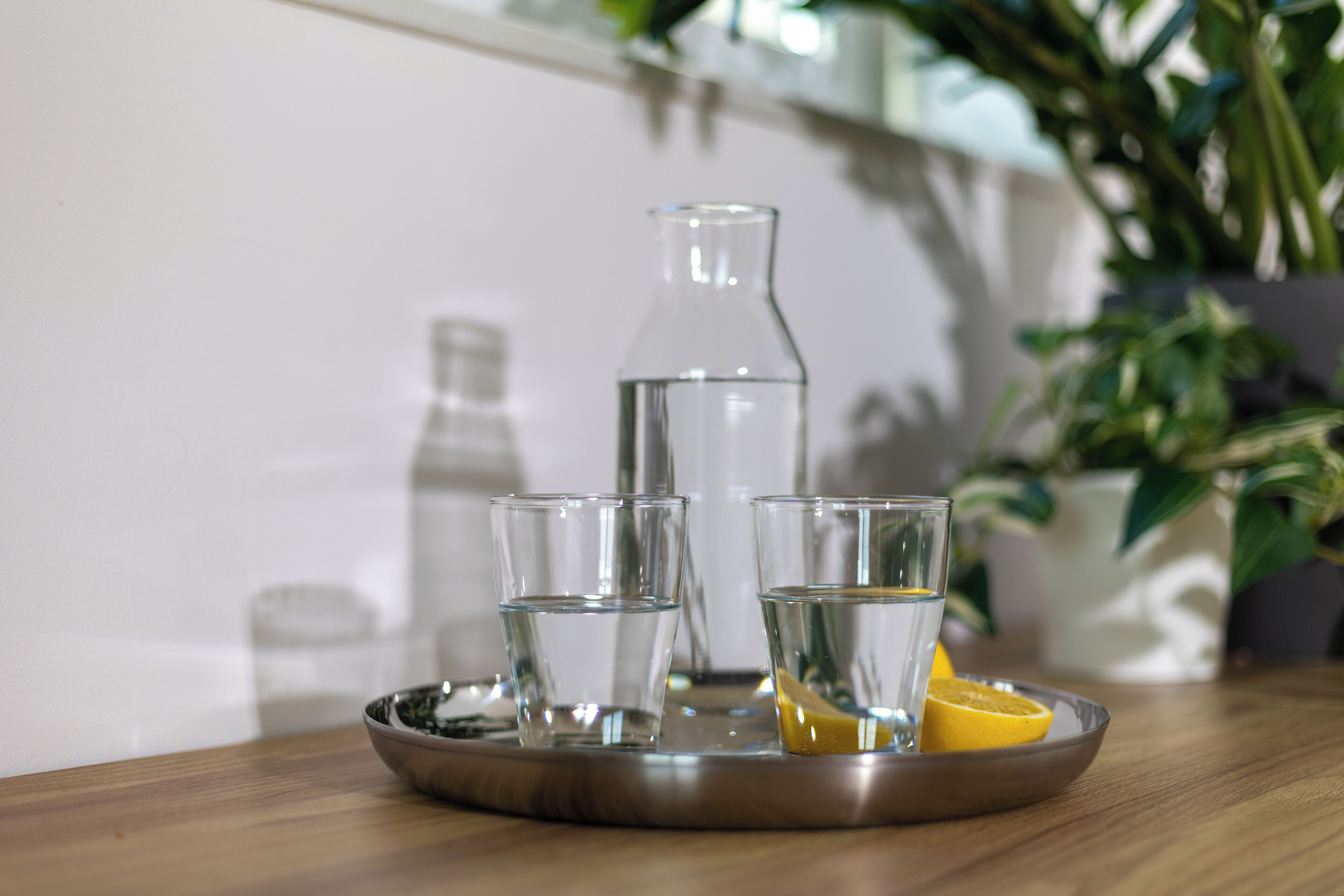 Een dienblad met een fles en glazen water, een schaal en een citroenpartje op een houten tafel.