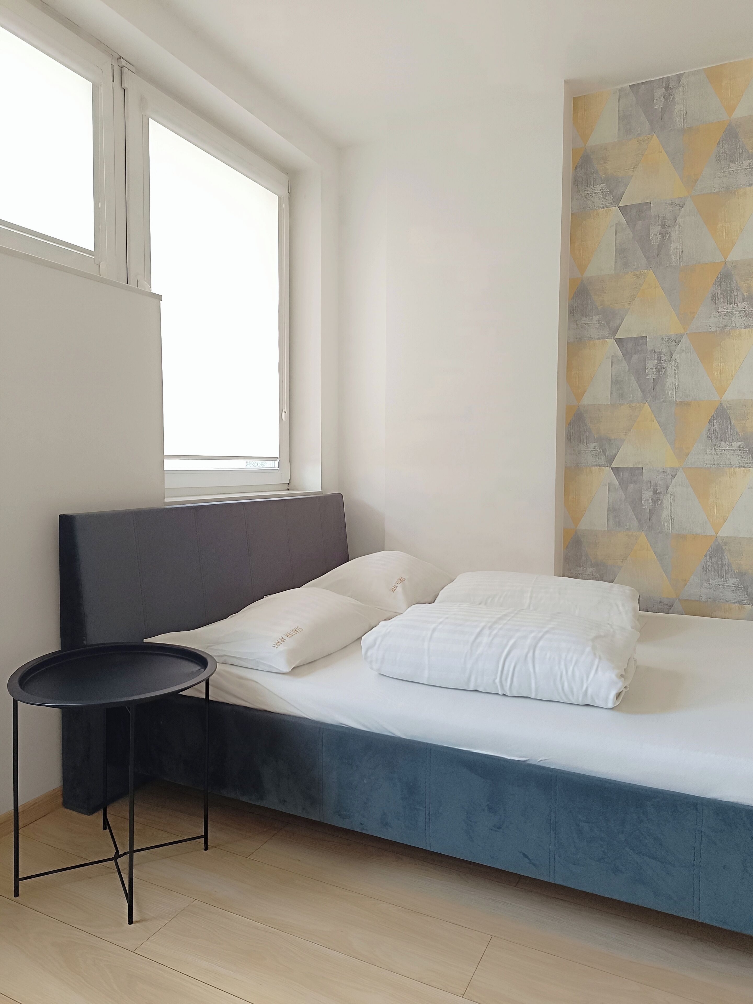 Un dormitorio moderno con cama, una mesita redonda y una ventana.