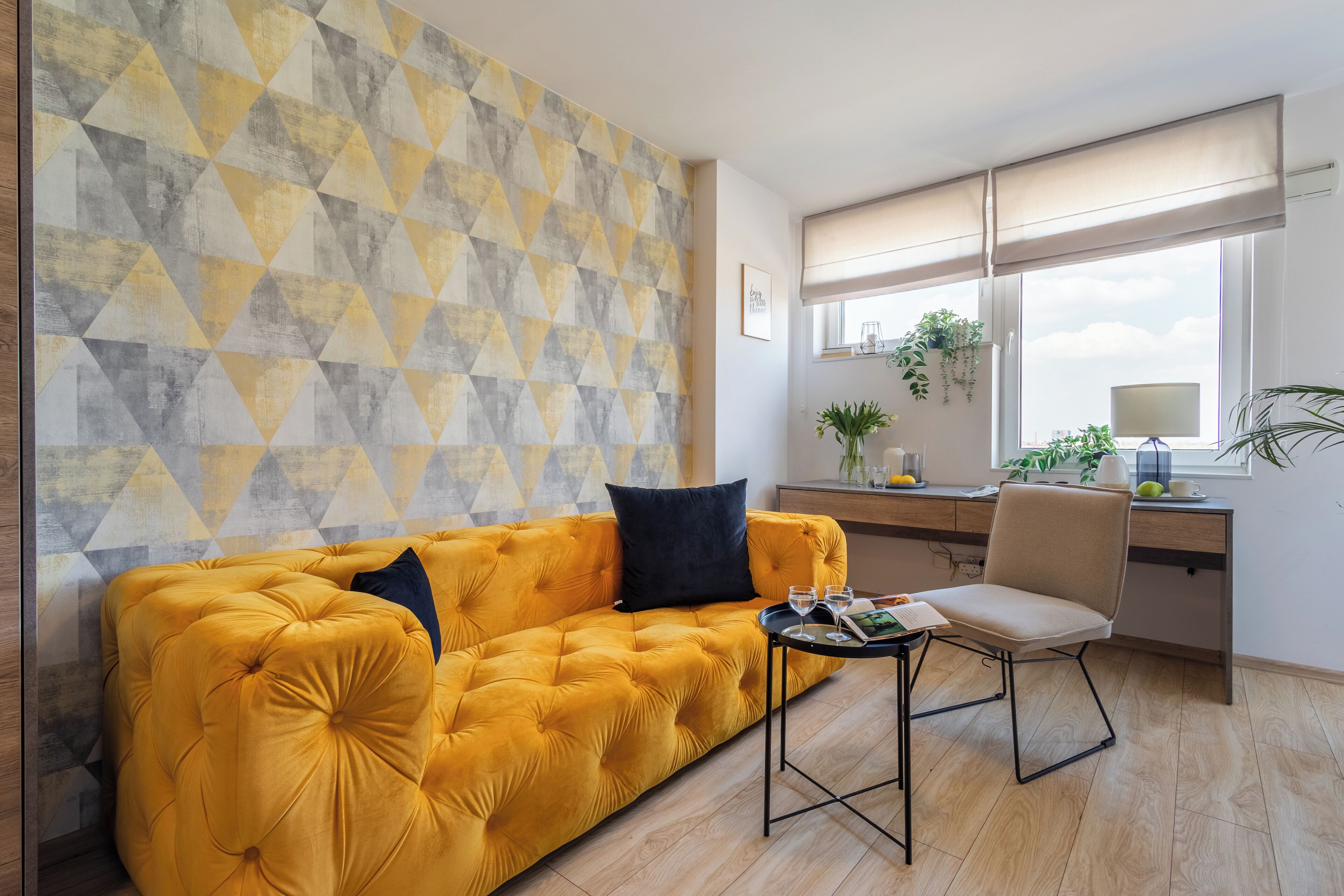 A modern living room with a yellow sofa, a small table, and a desk with a plant.