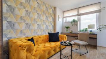 A modern living room with a yellow sofa, a small table, and a desk with a plant.