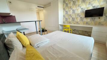 Quarto de hotel moderno com uma cama grande, uma escrivaninha, uma cadeira e uma TV fixada na parede.
