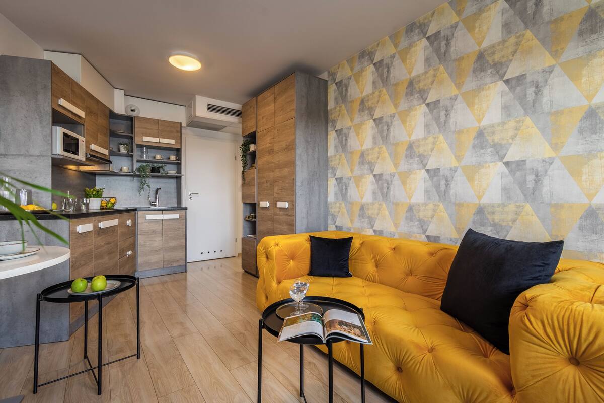 A modern kitchen with built-in appliances, a yellow sofa, and a geometric patterned wall.
