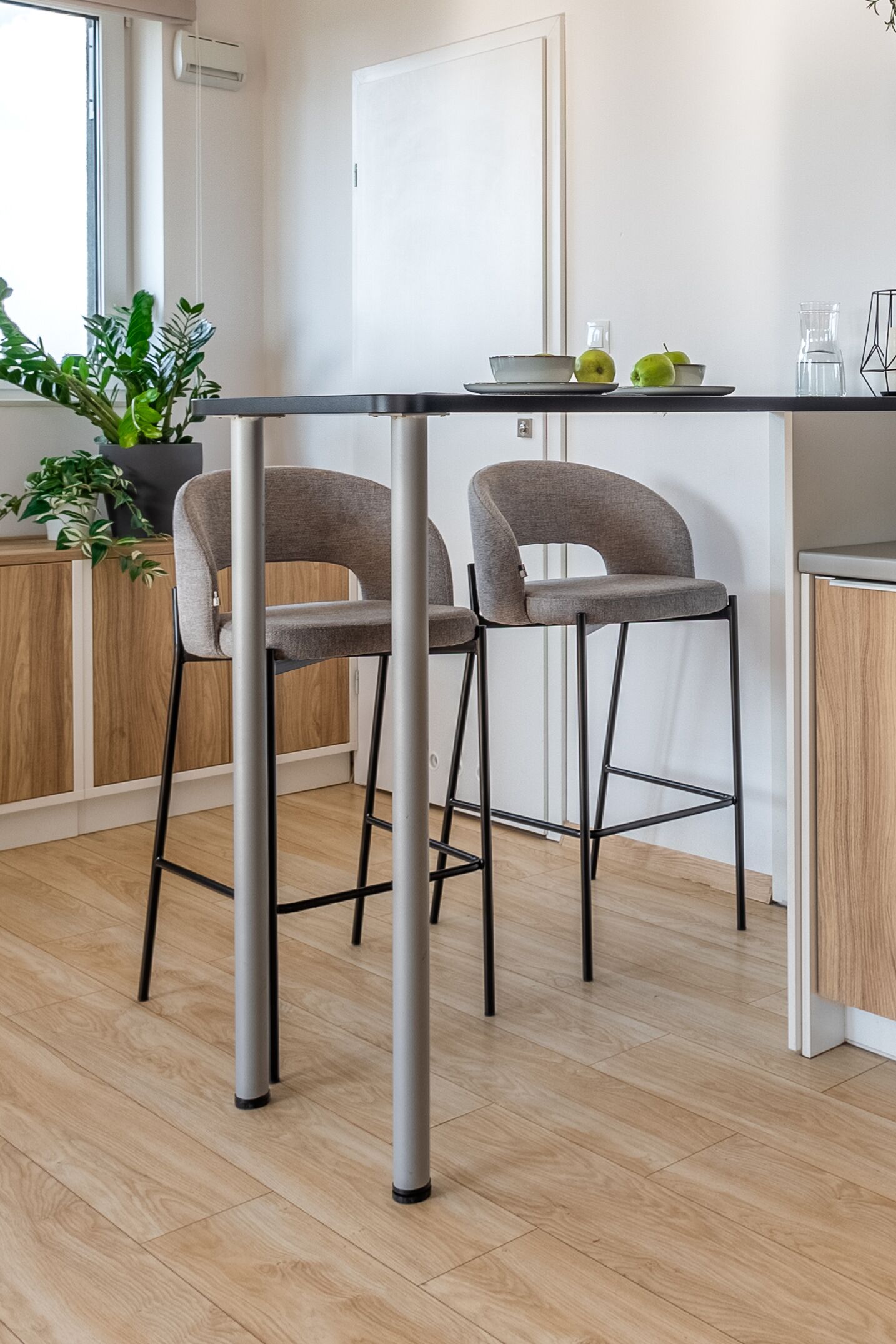 A modern kitchen with two grey bar stools, a white countertop, and a potted plant.