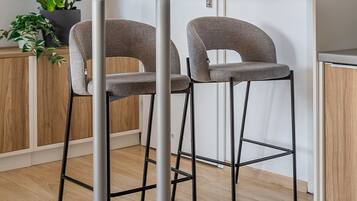 A modern kitchen with two grey bar stools, a white countertop, and a potted plant.