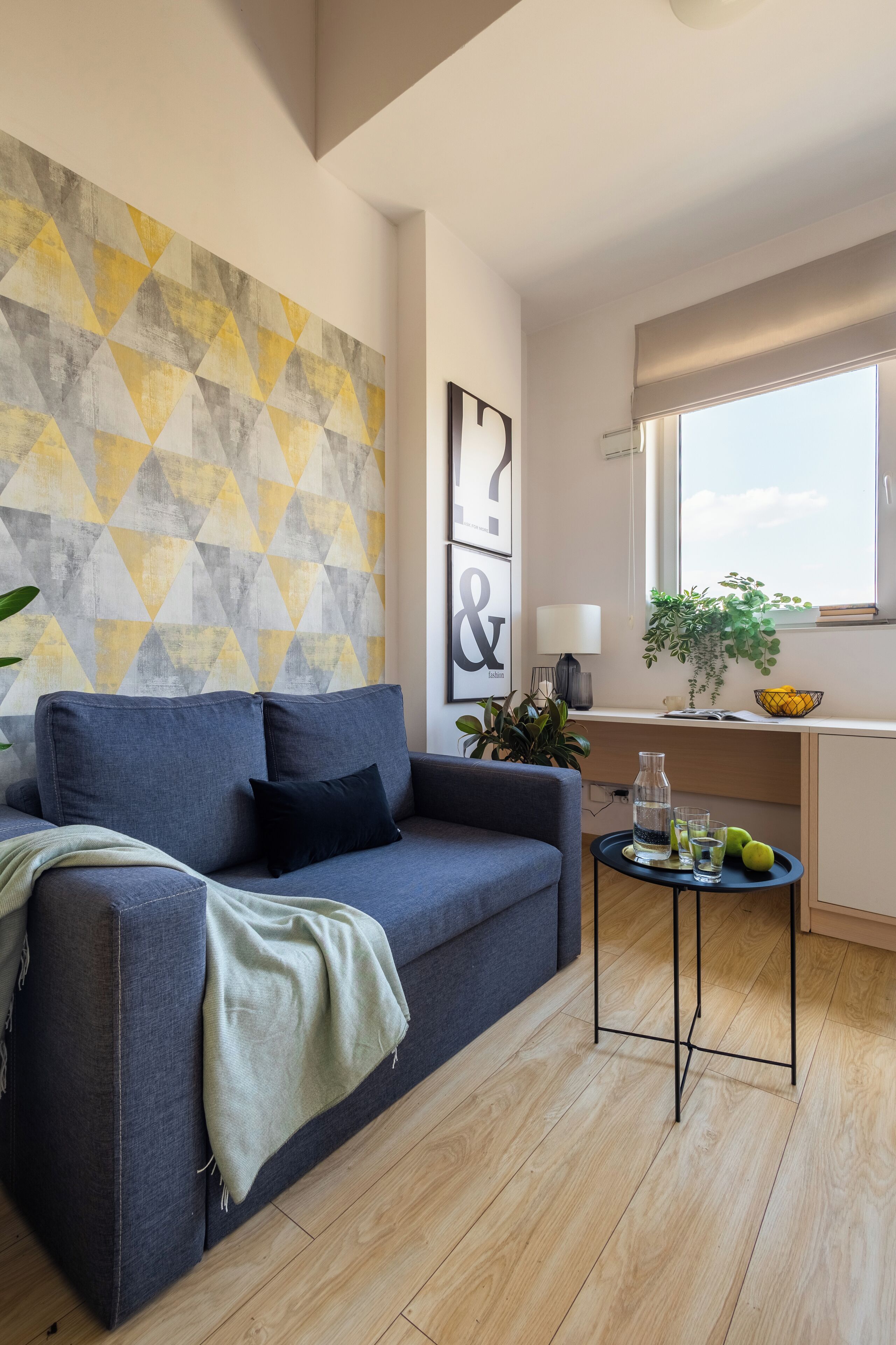 A modern living room with a grey sofa, a small side table, and a geometric patterned wall.
