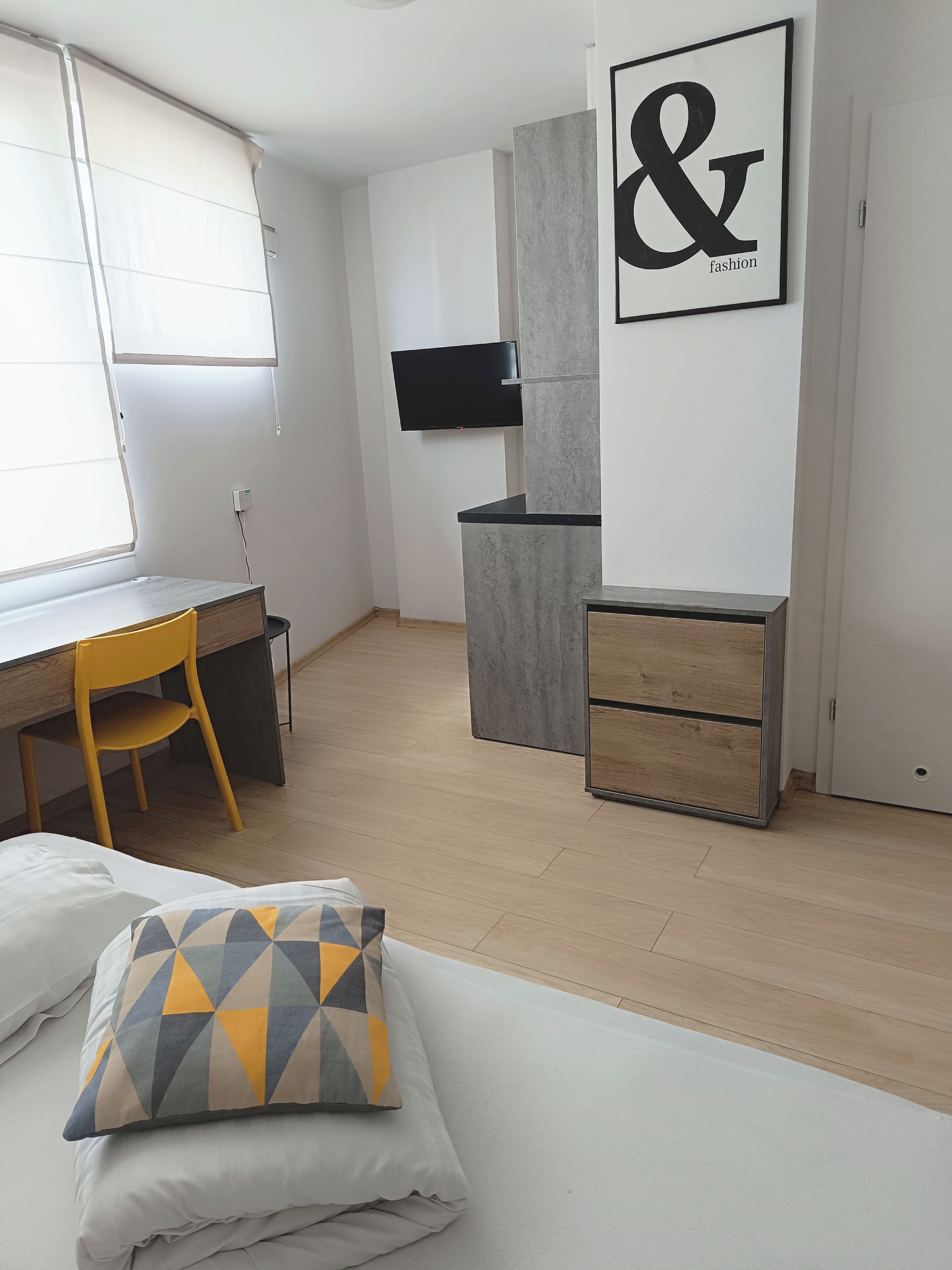 A modern bedroom with a bed, a desk, a chair, and a TV mounted on the wall.