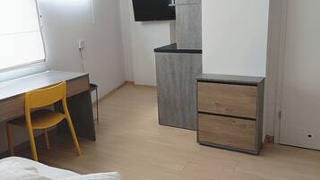 A modern bedroom with a bed, a desk, a chair, and a TV mounted on the wall.
