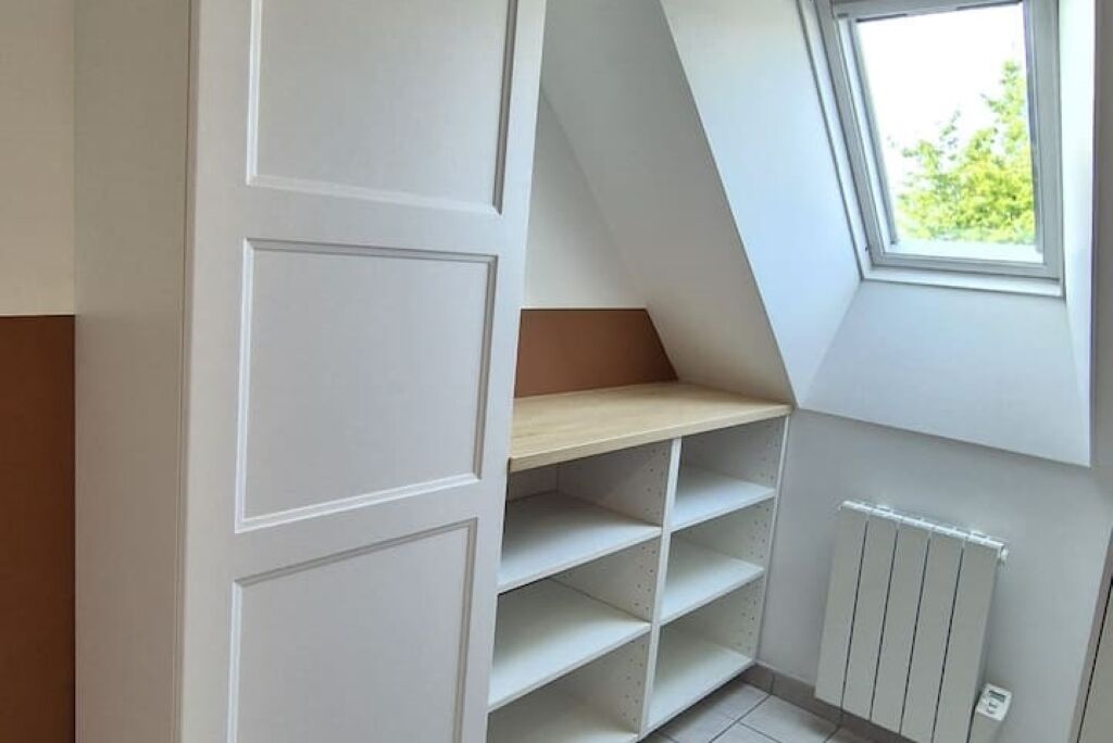 A room with a sloped ceiling, a window, and built-in shelving.