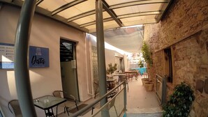 An outdoor cafe area with tables and chairs, a covered walkway, and a stone wall. - Data Maisonettes  (Chios)