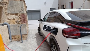 A white car parked in a driveway with a charging cable connected to it. - Data Maisonettes  (Chios)
