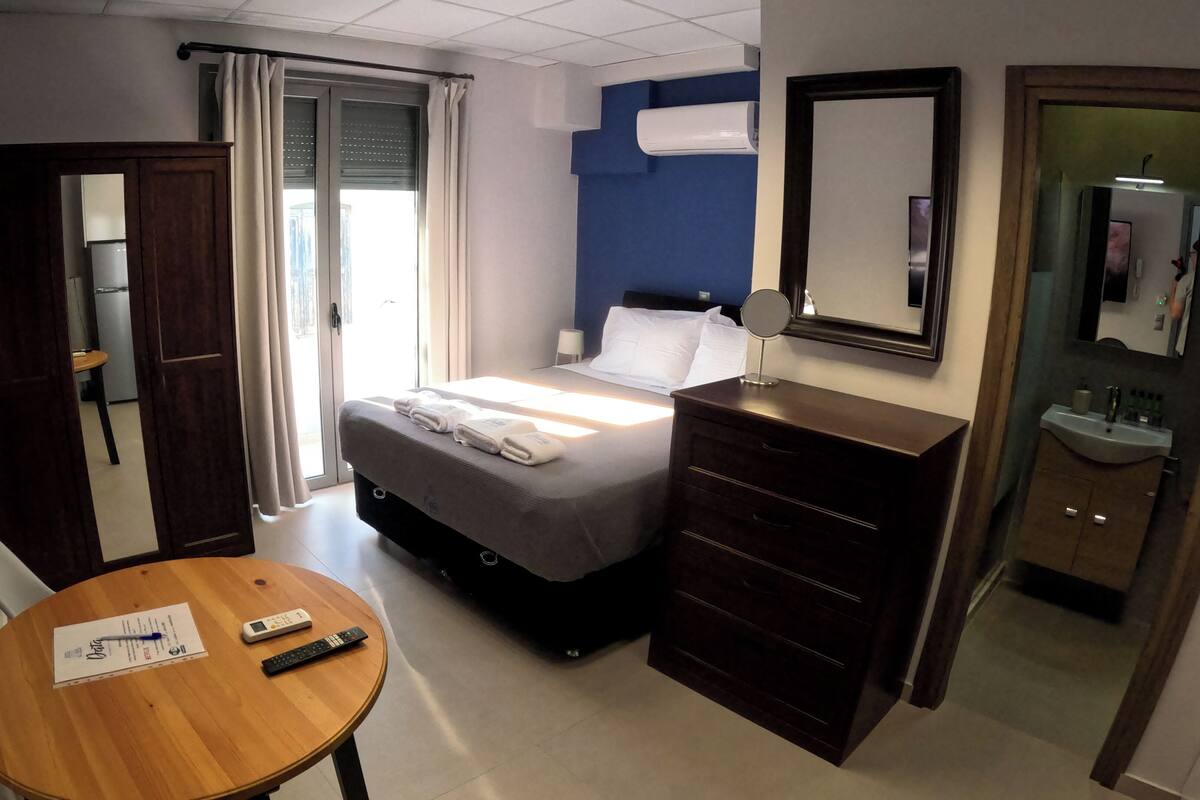 A hotel room with a bed, bedside table, dresser, and a bathroom with a sink and mirror.