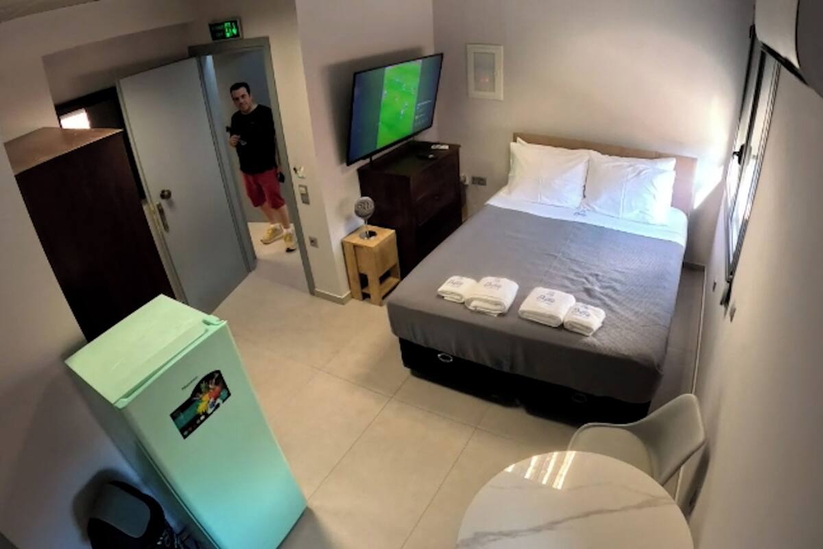 A hotel room with a bed, a television, a small table, and a refrigerator.
