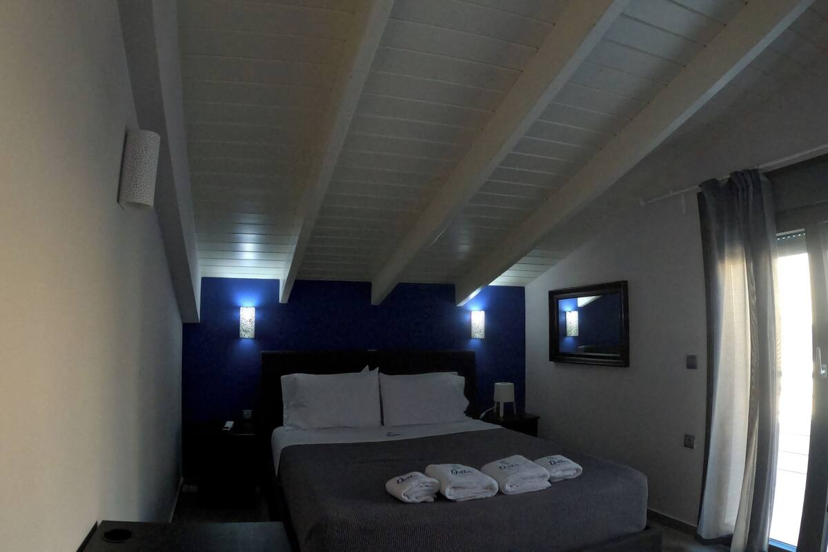 A hotel room with a bed, bedside tables, a nightstand, a mirror, and a window with curtains.