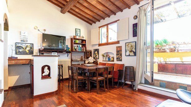 Ein gemütliches Zimmer mit Holzböden, einem Esstisch und Stühlen. Es gibt einen Fernseher, ein Bücherregal und verschiedene dekorative Gegenstände an den Wänden.