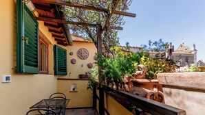 Ein Balkon mit Tisch und Stühlen, ein hölzernes Spalier und Blick auf ein historisches Gebäude im Hintergrund.