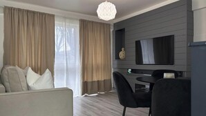 Un salon moderne comprenant un canapé, une table à manger avec des chaises, un téléviseur fixé au mur et un lustre.