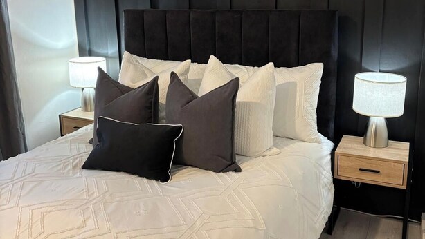 Une chambre à coucher moderne avec une tête de lit sombre, un grand lit doté de nombreux oreillers et des lampes de chevet.