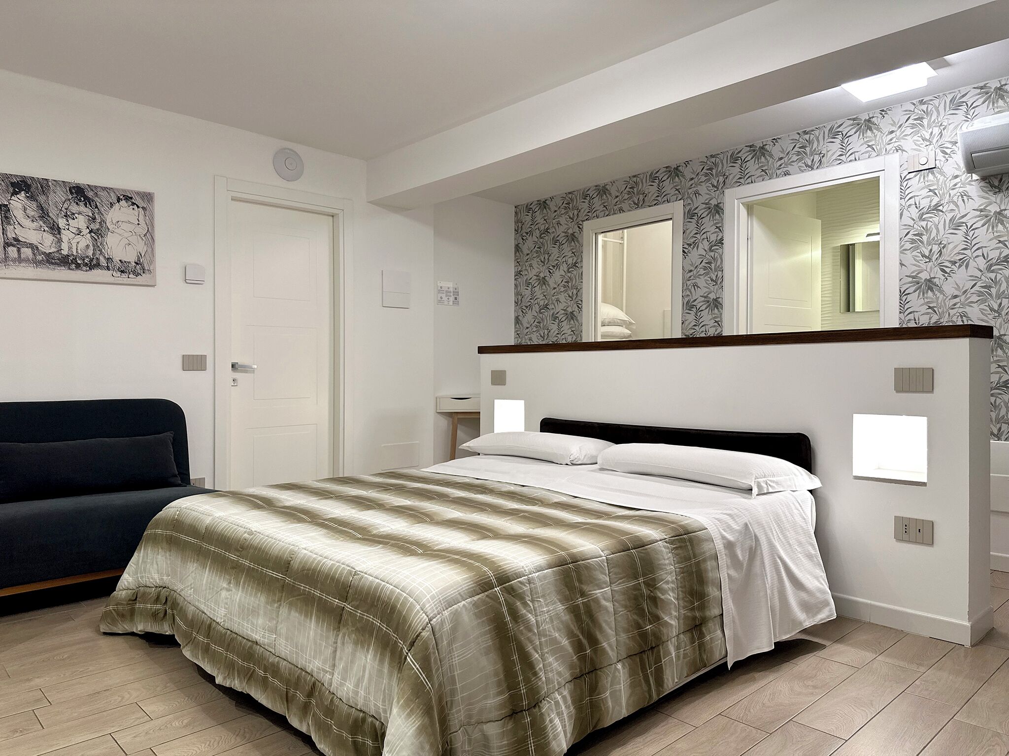 Un dormitorio con cama, una silla, una puerta, un espejo y una pared con estampado floral.