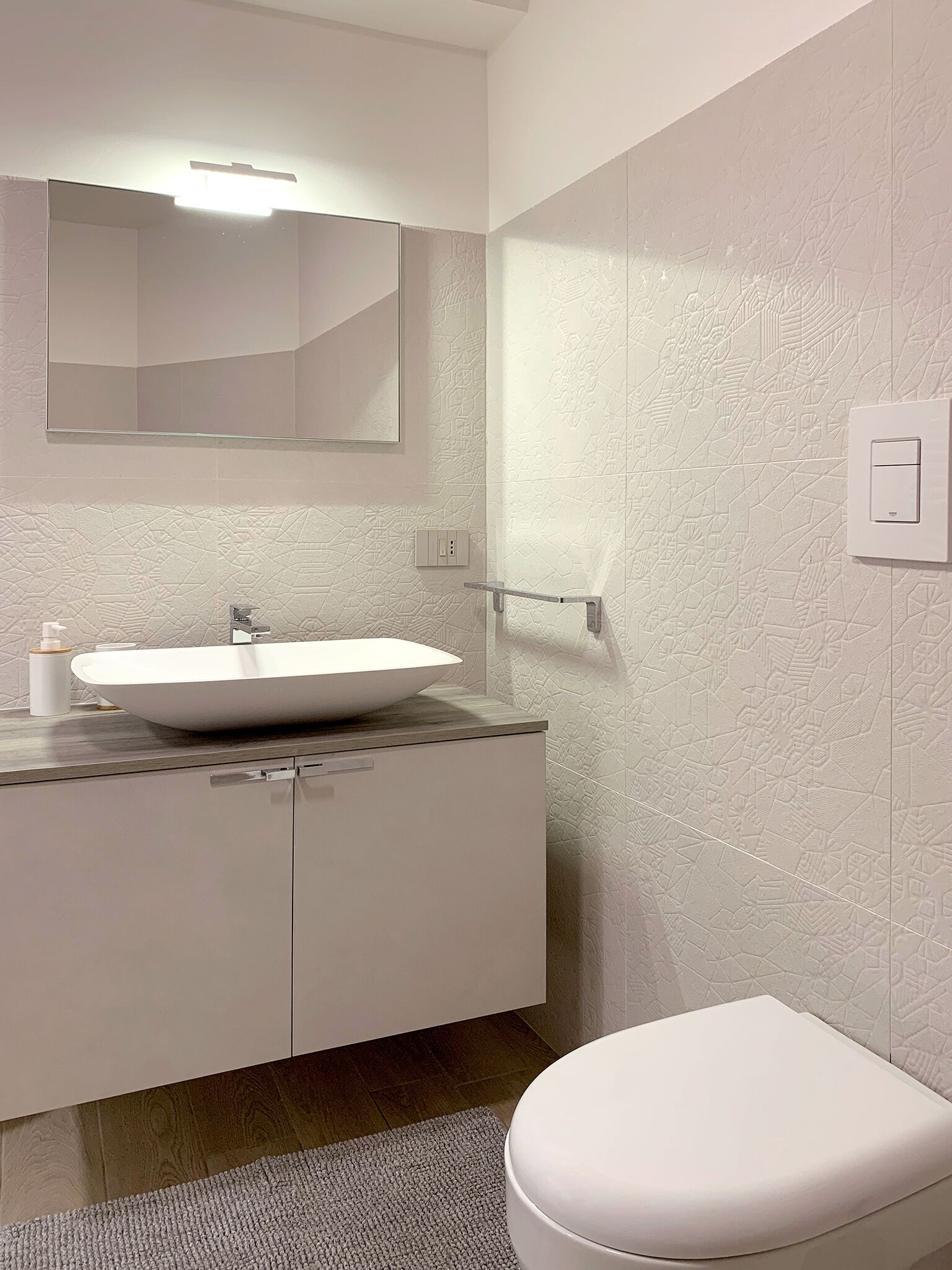 Uma casa de banho moderna com lavatório branco, espelho e sanita.