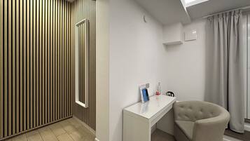 Ein modernes Zimmer mit einer Wand aus Holzlamellen, einem weißen Schreibtisch, einem gepolsterten Sessel und einem Fenster mit Vorhängen.