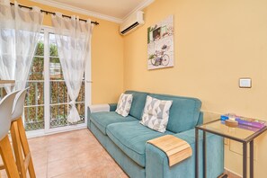Una habitación con un sofá azul verdoso, una mesa de vidrio con una caja de acertijos y una ventana con cortina.