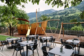 An outdoor patio with tables and chairs, a wooden play structure, and a view of a mountainous landscape. - Holiday Apartment 'Riffl Anna' with Mountain View, Balcony and Wi-Fi (Riffian)