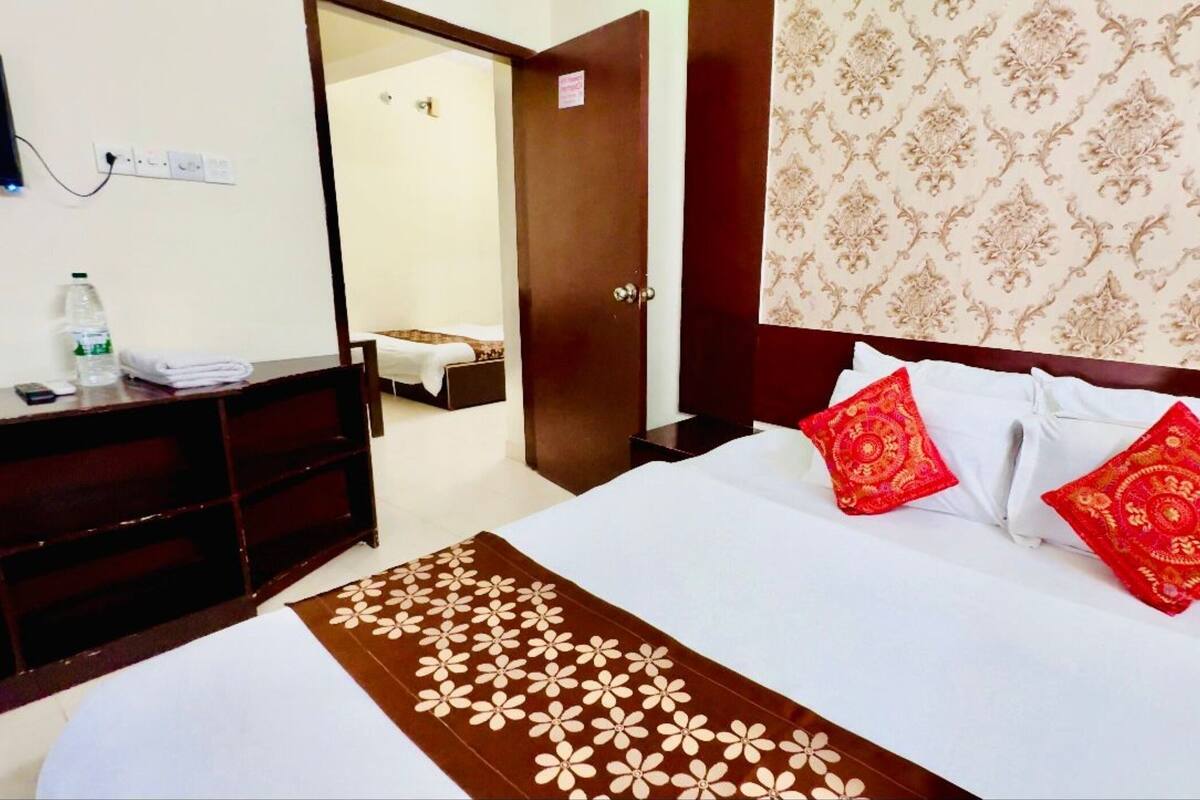 Een hotelkamer met een bed, een bureau, een stoel, een nachtkastje, een spiegel en een deur naar een andere kamer.