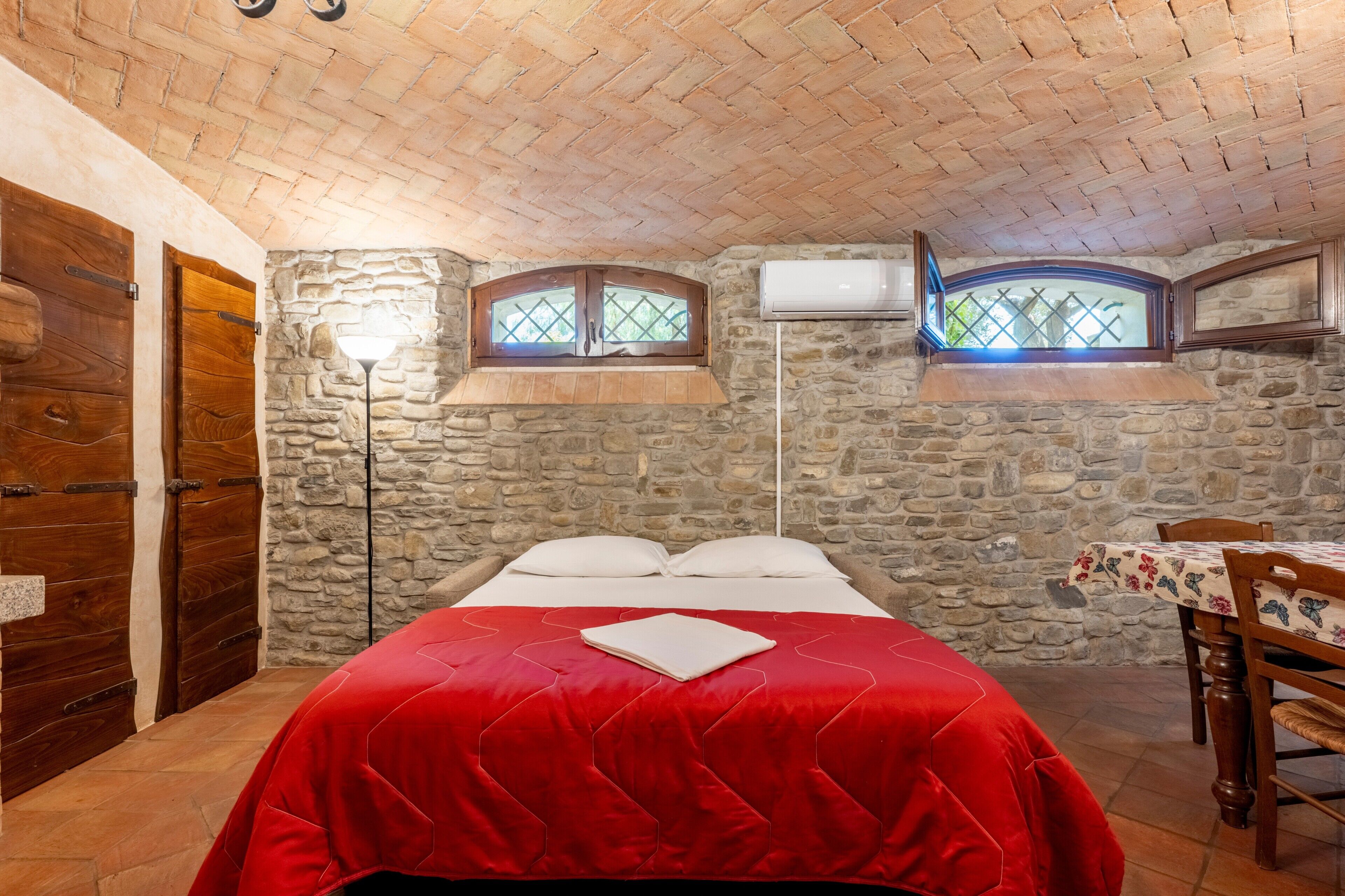 Un dormitorio con pared de piedra, puerta de madera y cama con manta roja.