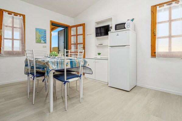 A room with a dining table, chairs, a kitchen area with a microwave, and a refrigerator.