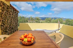 A wooden table with a fruit bowl, a white chair, and a view of a mountainous landscape.