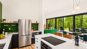 A modern kitchen with a built-in stove, a large refrigerator, and a dining area with a view of the outdoors. - Scandinavian Chalet | Games | Hot Tub/Sauna (Dansville)