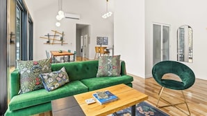 A modern living room with a green sofa, a wooden coffee table, and a green chair. There is a dining area in the background with a wooden table and chairs. - Scandinavian Chalet | Games | Hot Tub/Sauna (Dansville)