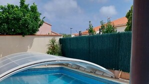 Una piscina con agua cristalina azul, rodeada de baldosas de piedra y sillas de descanso blancas.