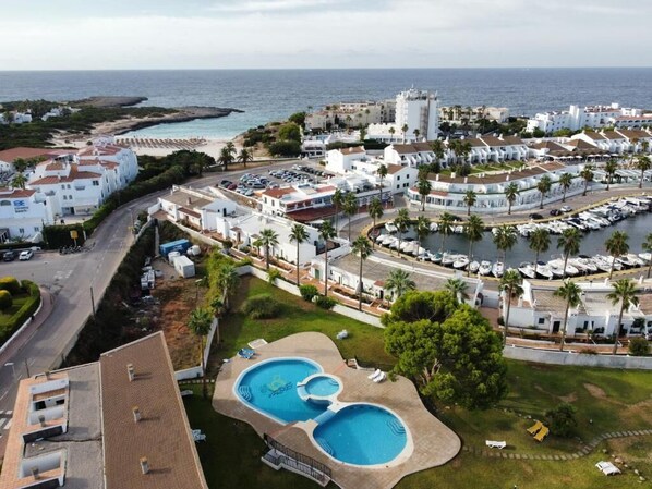 Un complejo turístico en la costa con piscina, edificios blancos y vistas al mar.